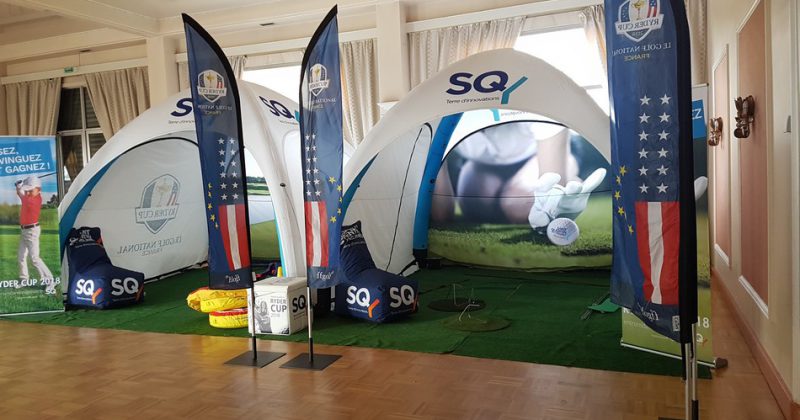 Stand d'exposition pour la Ryder Cup avec tentes, drapeaux et décor de golf.