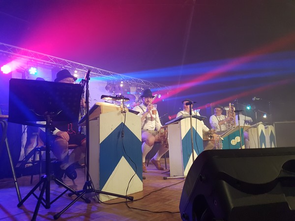 Musiciens en costume jouent sur scène, éclairés par des lumières colorées dans une ambiance festive.