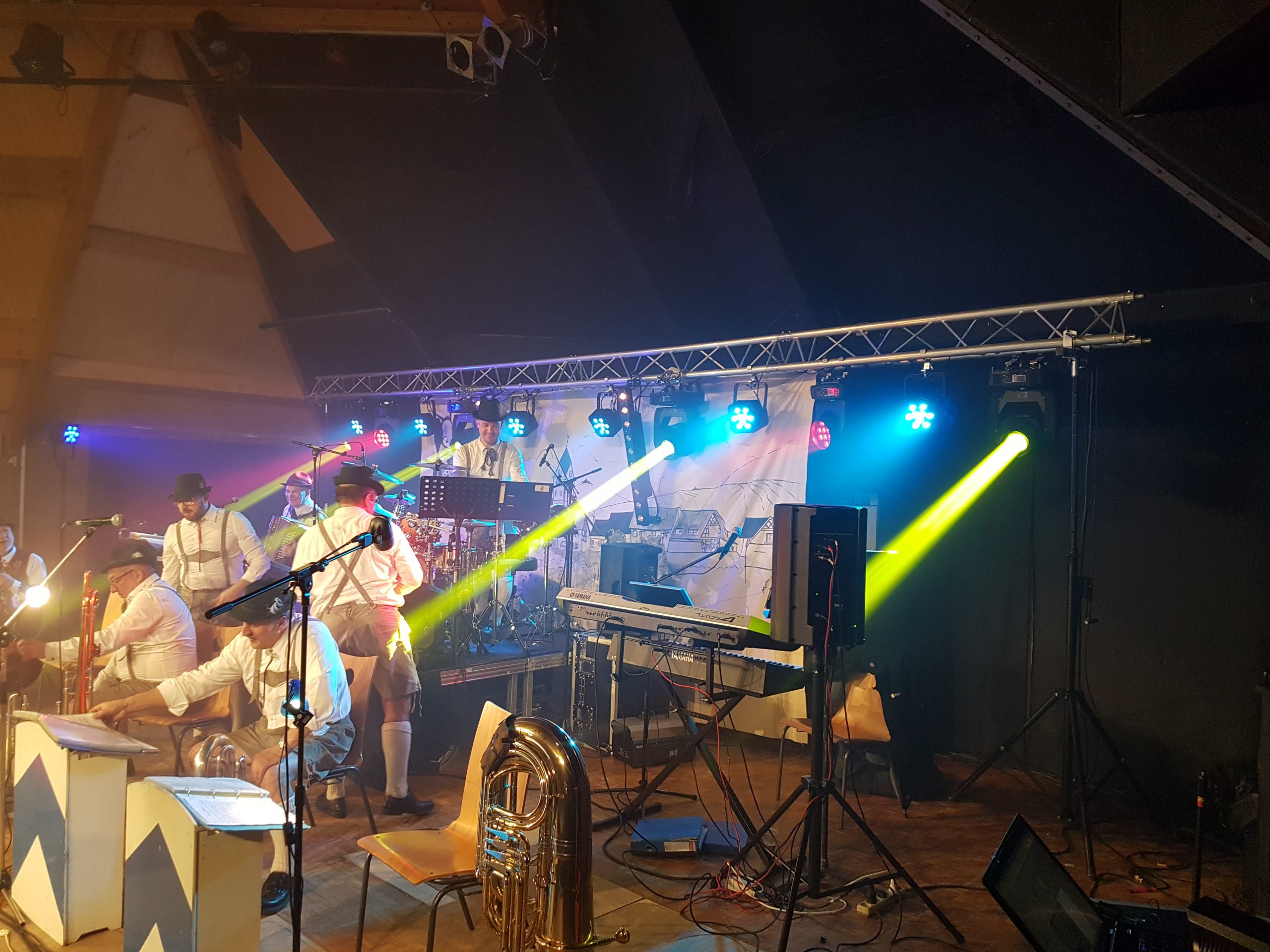 Concert en direct avec plusieurs musiciens sur scène, éclairage coloré et matériel de sonorisation.