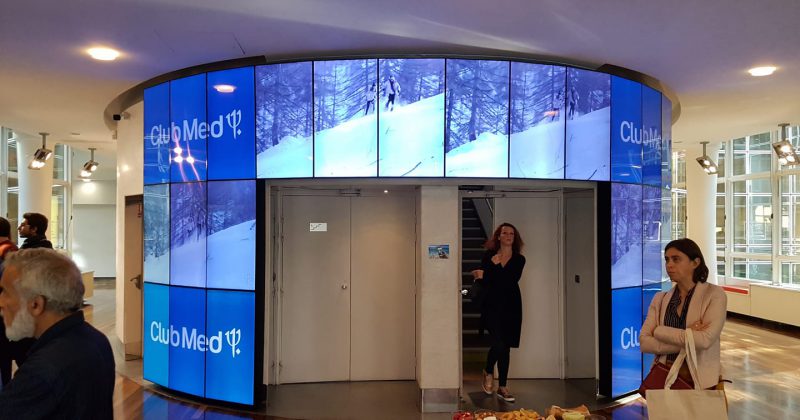 Hall d'accueil du siège social du Club Med avec un écran vidéo montrant des paysages enneigés et des visiteurs.