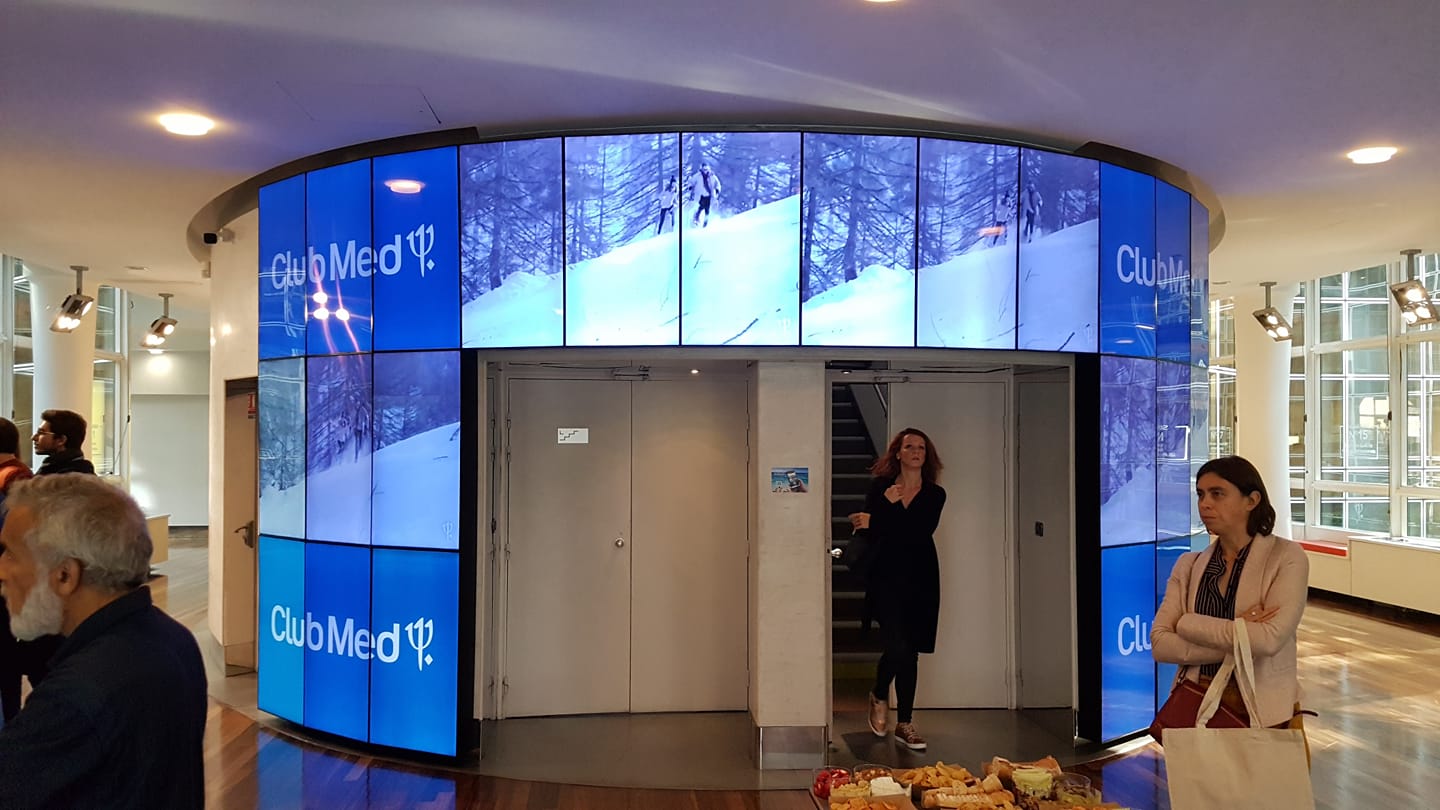 Hall d'accueil du siège social du Club Med avec un écran vidéo montrant des paysages enneigés et des visiteurs.