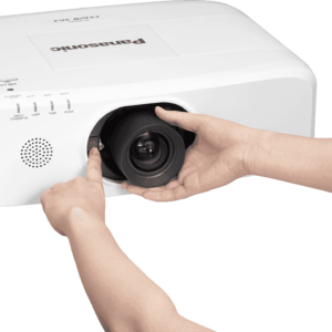 Main droite insérant un objectif dans un projecteur Panasonic.