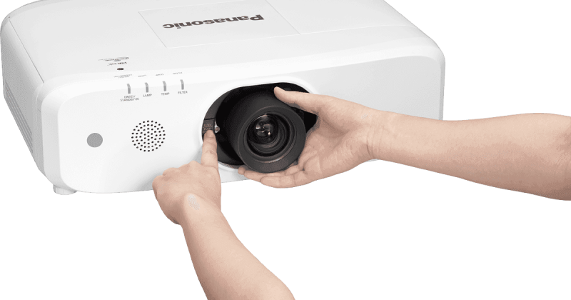 Main droite insérant un objectif dans un projecteur Panasonic.