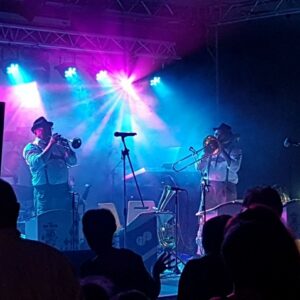Concert de l'Orchestre Max Fahren avec des musiciens jouant sous des lumières colorées, captivant le public.