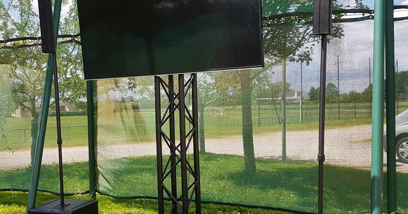 Écran de télévision monté sur trépied, entouré de deux haut-parleurs, en extérieur lors de la retransmission de Roland Garros 2019.