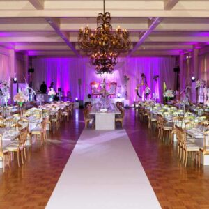 Décor élégant d'un salon avec tables dorées, éclairage rose et arrangement floral pour un événement festif.