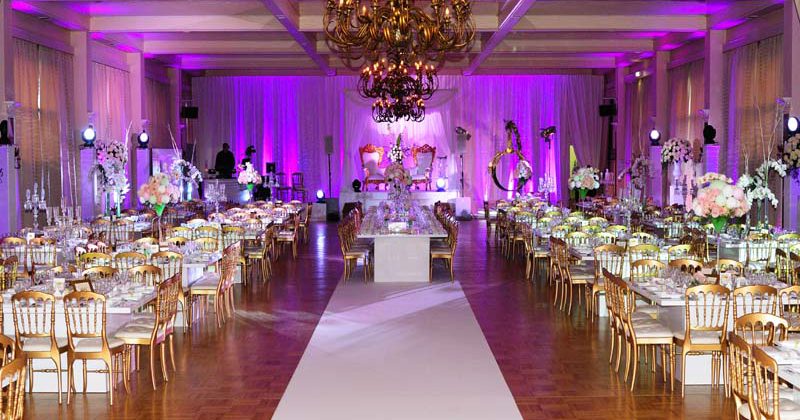 Décor élégant d'un salon avec tables dorées, éclairage rose et arrangement floral pour un événement festif.