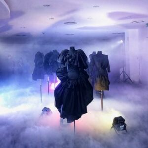 Robe noire présentée dans un espace brumeux, avec éclairage coloré et mannequins stylisés lors de l'événement mode avec Xuan.