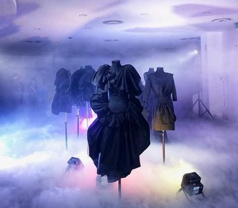 Robe noire présentée dans un espace brumeux, avec éclairage coloré et mannequins stylisés lors de l'événement mode avec Xuan.