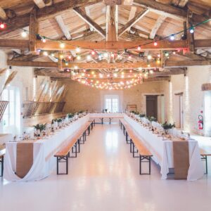 Salle de réception élégamment décorée pour un mariage, avec tables dressées et guirlandes lumineuses.