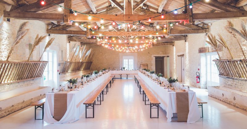 Salle de réception élégamment décorée pour un mariage, avec tables dressées et guirlandes lumineuses.