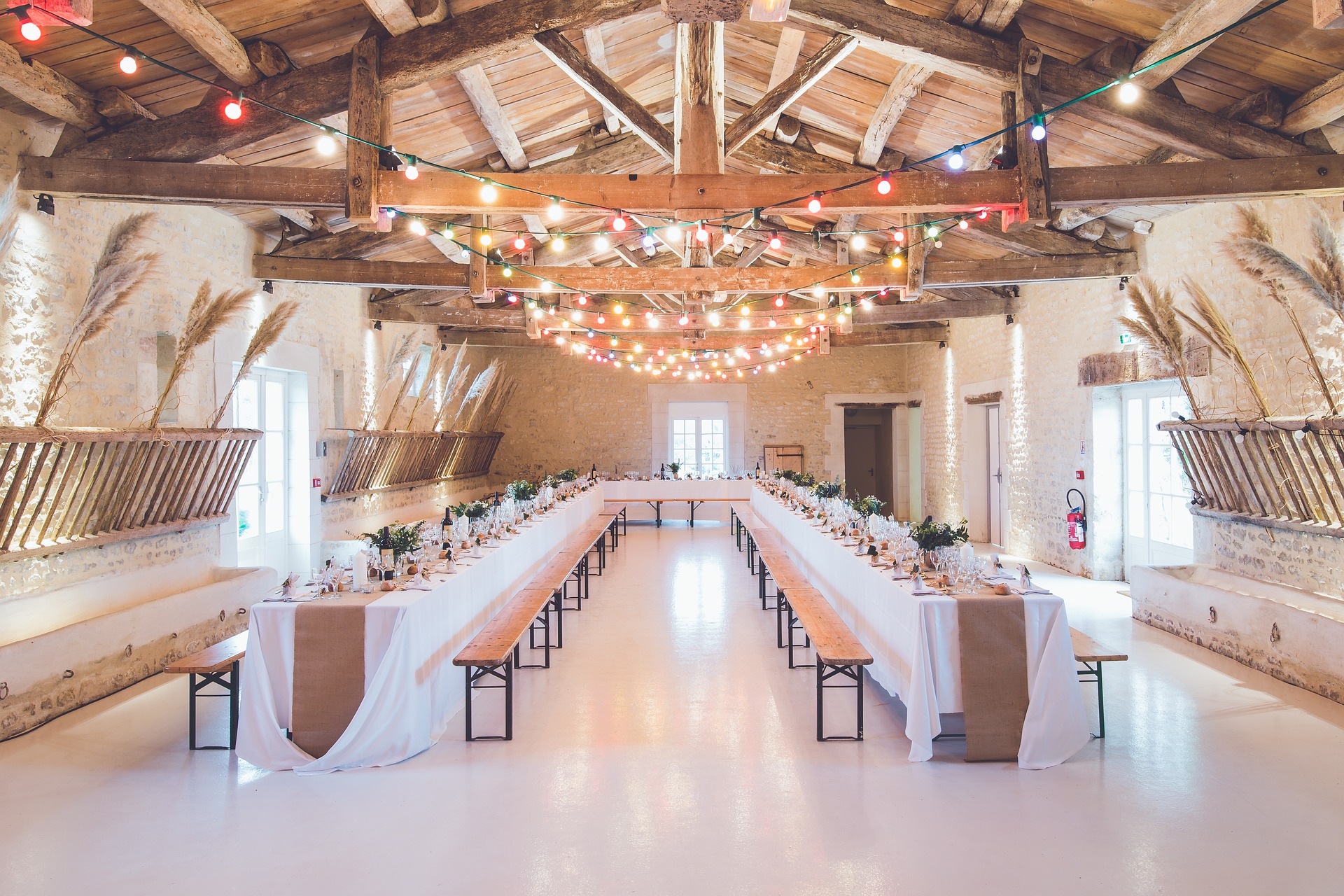 Salle de réception élégamment décorée pour un mariage, avec tables dressées et guirlandes lumineuses.