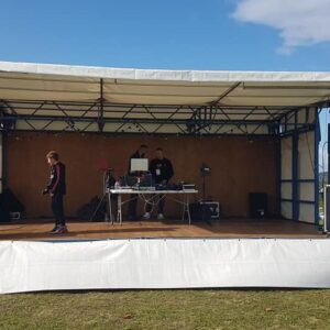 Scène mobile installée sur un terrain de foot, équipée pour sonorisation d'événements, avec des DJ en action.