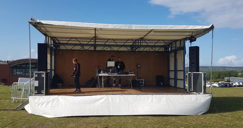Scène mobile installée sur un terrain de foot, équipée pour sonorisation d'événements, avec des DJ en action.
