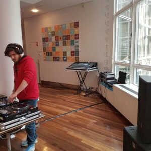 Un DJ mixe sur des platines dans un espace avec plusieurs équipements audio et un mur décoré.