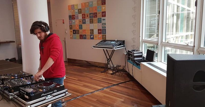 Un DJ mixe sur des platines dans un espace avec plusieurs équipements audio et un mur décoré.