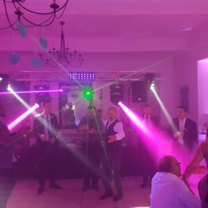 Danse festive lors d'un mariage, éclairage coloré et ambiance survoltée, avec des invités en costume.