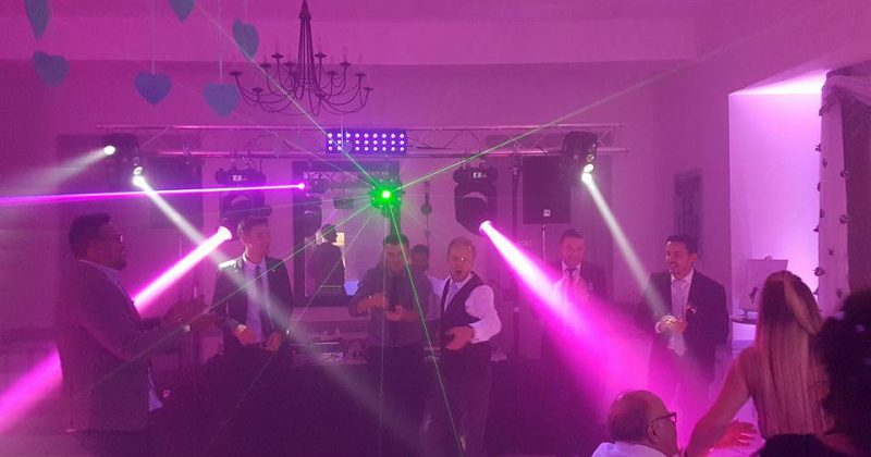 Danse festive lors d'un mariage, éclairage coloré et ambiance survoltée, avec des invités en costume.