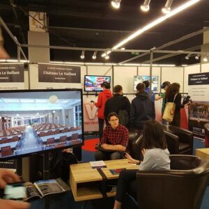 Salon Studyrama avec des stands d'écoles, des visiteurs et un écran présentant le Château Le Vaillant.