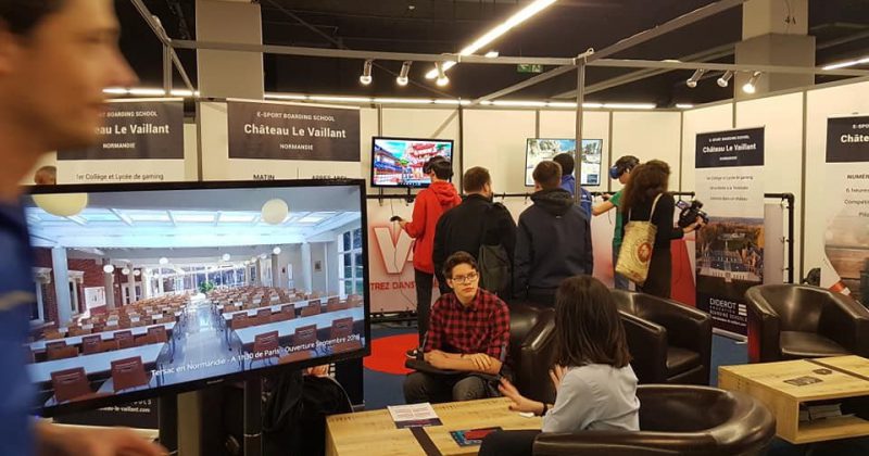 Salon Studyrama avec des stands d'écoles, des visiteurs et un écran présentant le Château Le Vaillant.