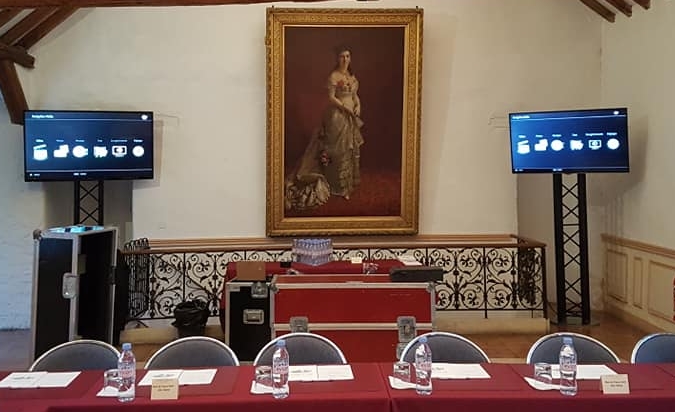 Installation de quatre écrans sur totem pour un événement, avec une table et des chaises dans un cadre décoratif.