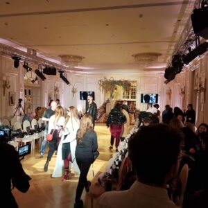 Défilé de mode au Ritz, avec des personnes se préparant et une scène illuminée, capturant l'atmosphère élégante de l'événement.