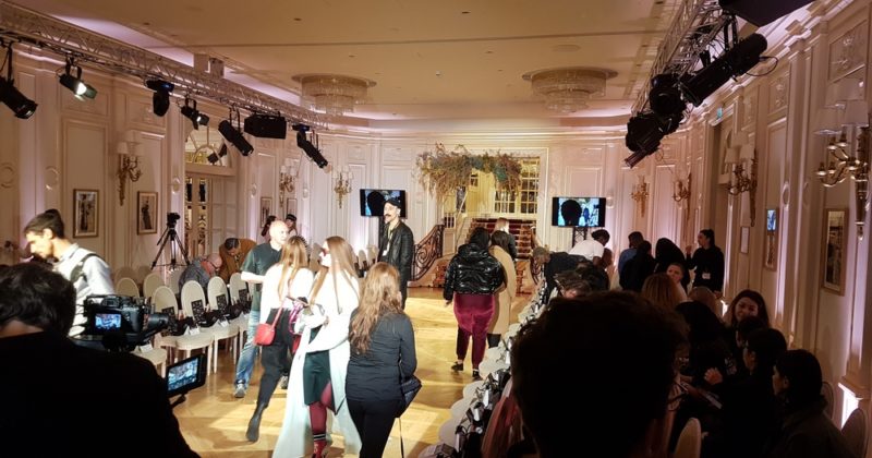 Défilé de mode au Ritz, avec des personnes se préparant et une scène illuminée, capturant l'atmosphère élégante de l'événement.