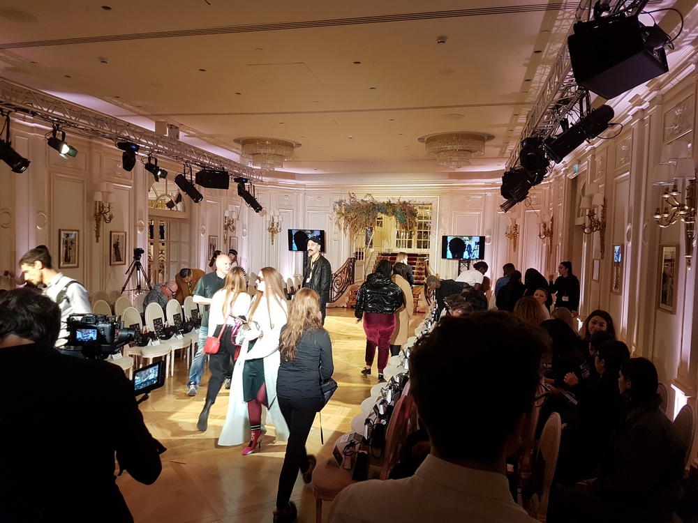 Défilé de mode au Ritz, avec des personnes se préparant et une scène illuminée, capturant l'atmosphère élégante de l'événement.