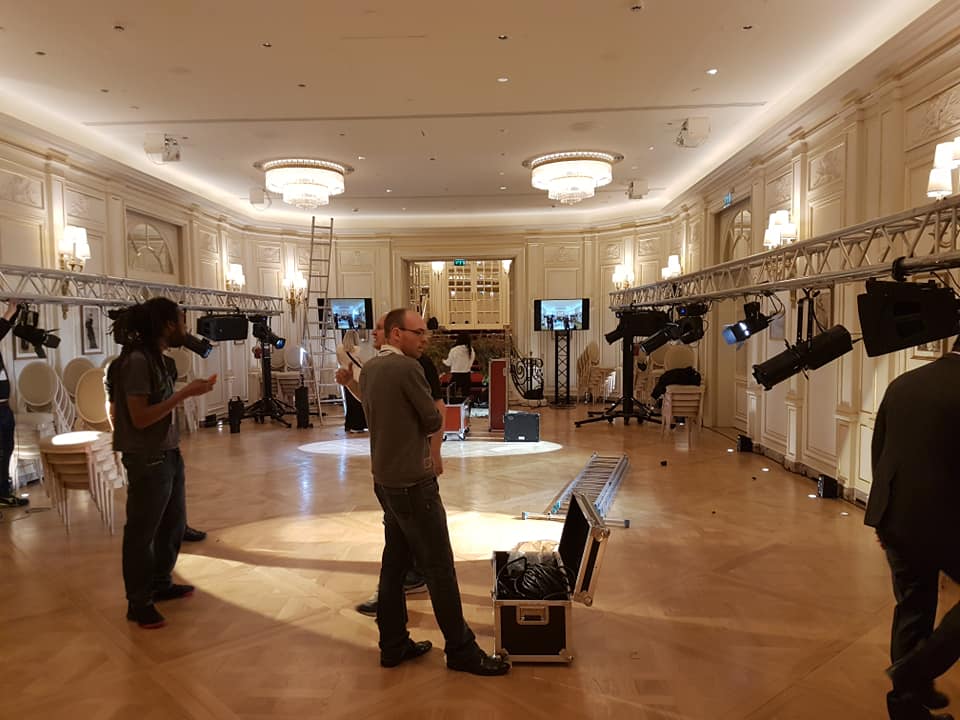 Installation en cours pour un défilé de mode au Ritz, avec matériel de son et éclairage. Equipe en action dans une salle élégante.