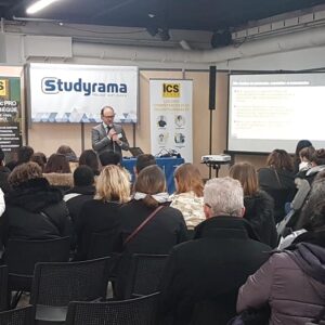 Conférence au salon d'expo Espace Champerret, avec un intervenant devant un public attentif et des présentations en arrière-plan.