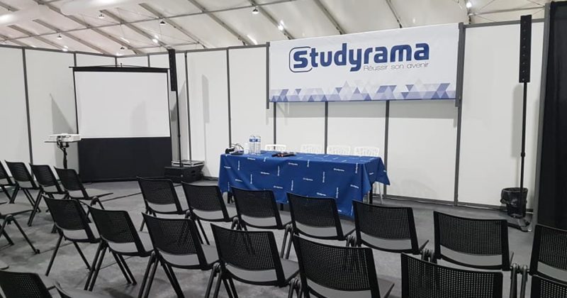 Salle de conférence avec chaises disposées, écran projeté et table pour l'événement Symbiose à Paris, 23 novembre 2019.