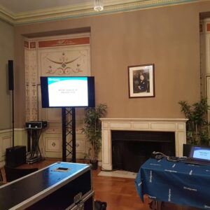Salle de conférence avec équipement audiovisuel et présentation sur un écran, décorée et équipée pour un événement.