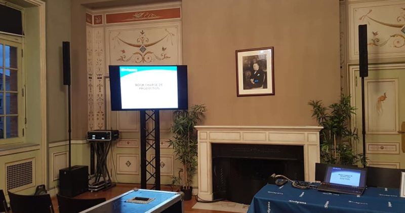 Salle de conférence avec équipement audiovisuel et présentation sur un écran, décorée et équipée pour un événement.