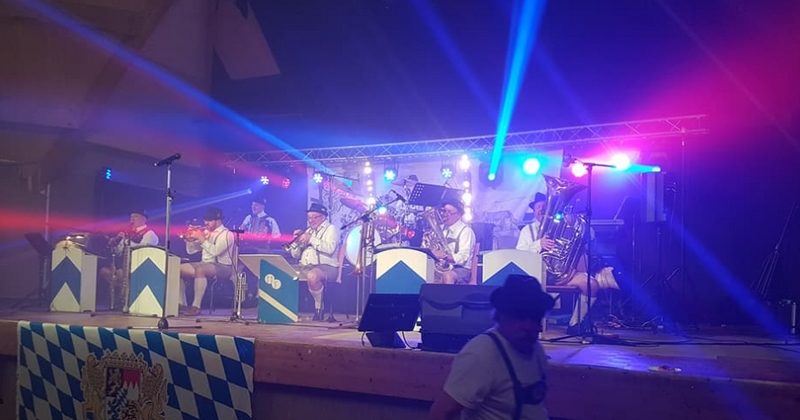 Concert avec des musiciens en tenue traditionnelle, éclairage coloré et équipements de sono sur scène.
