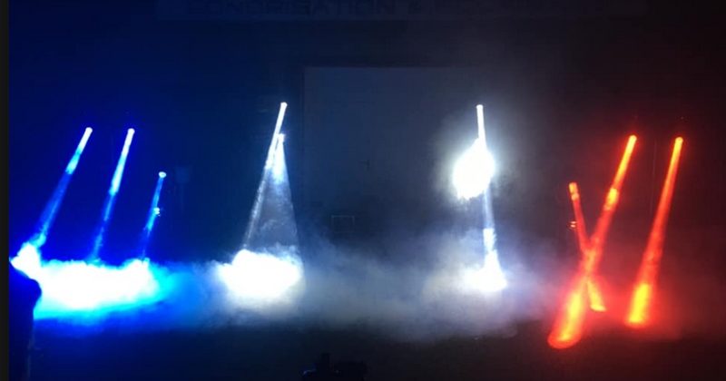 Spectacle lumineux en hommage aux soignants, avec faisceaux lumineux bleus et rouges dans une ambiance brumeuse.