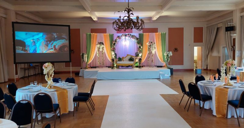 Décor coloré d'un mariage indien à la salle Saint-Exupéry, avec scène, tables et projecteur le 3 juillet 2021.