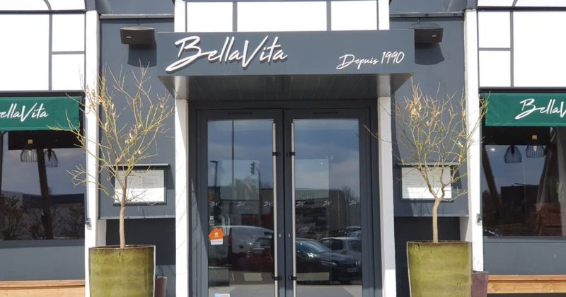 Entrée du restaurant BellaVita à Coignières, avec des pots de fleurs et une enseigne élégante.