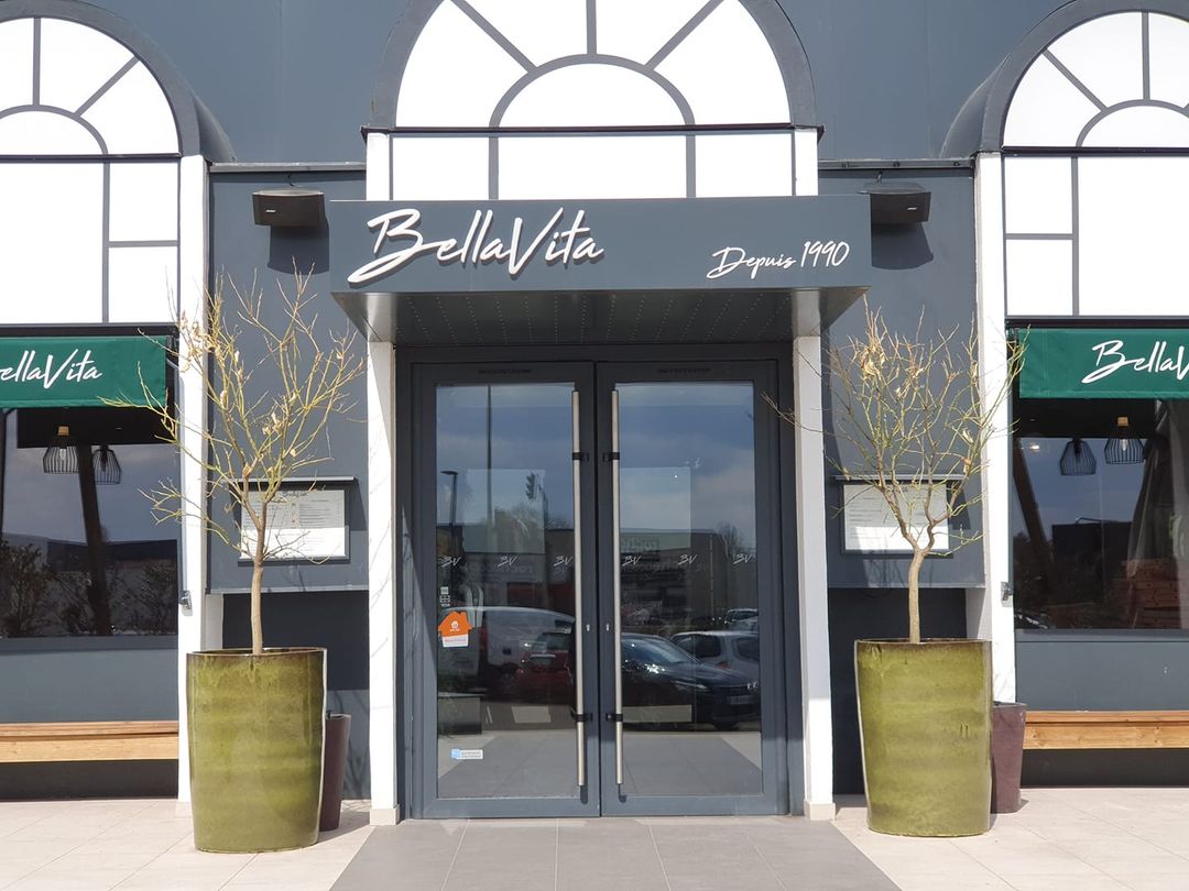 Entrée du restaurant BellaVita à Coignières, avec des pots de fleurs et une enseigne élégante.