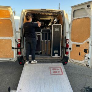Technicien au chargement de matériel audio-visuel dans une camionnette, préparant un événement.