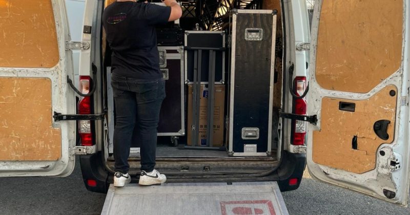 Technicien au chargement de matériel audio-visuel dans une camionnette, préparant un événement.