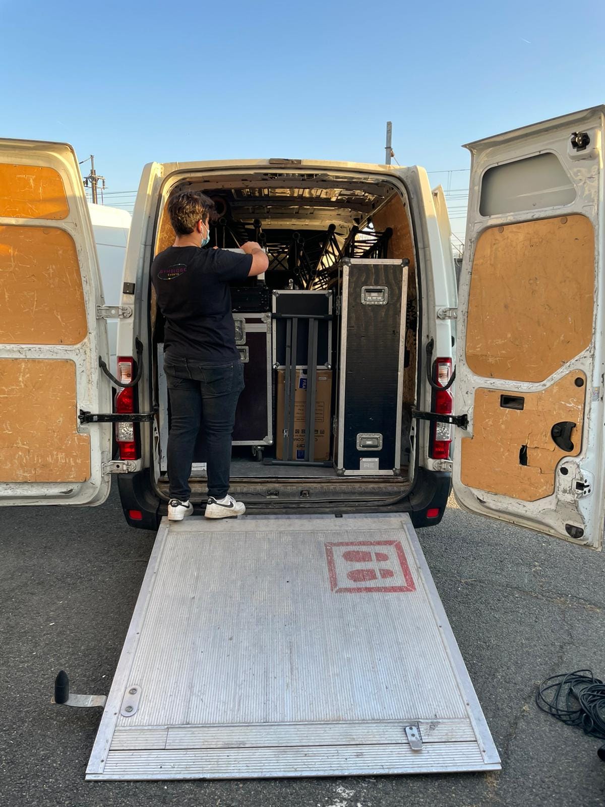 Technicien au chargement de matériel audio-visuel dans une camionnette, préparant un événement.