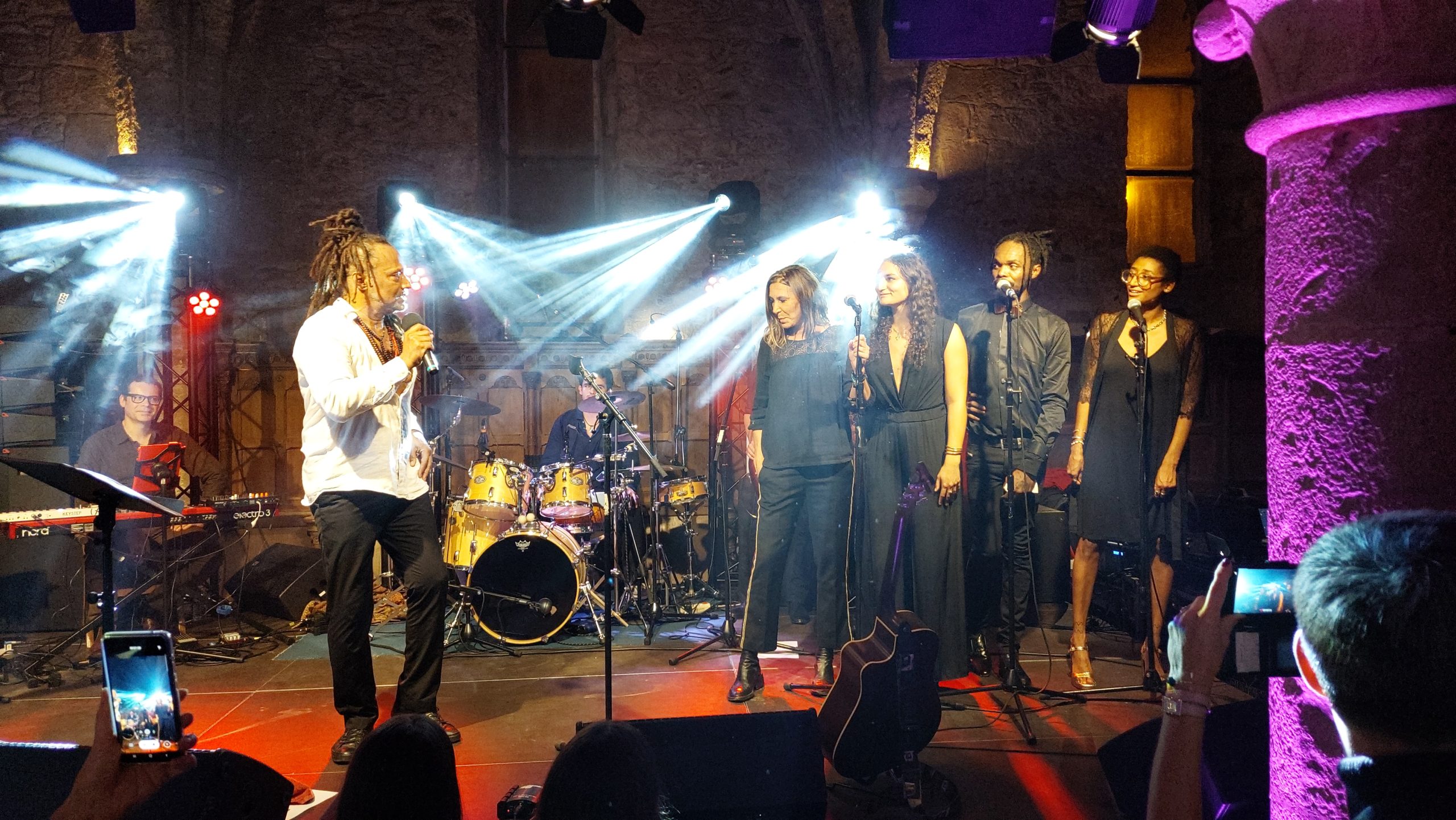 Concert du 30 novembre 2021 avec plusieurs artistes sur scène, éclairage dynamique, musicien au clavier en arrière-plan.