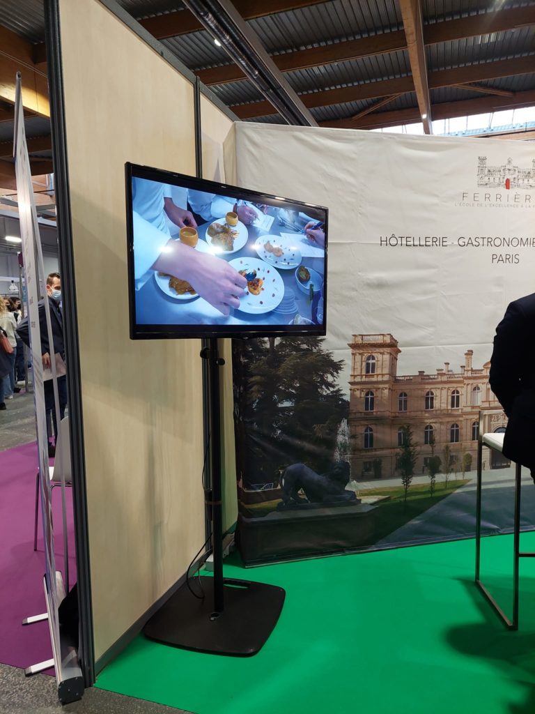 Écran montrant des plats raffinés lors d'un événement gastronomique au stand de l'école Ferrier à Paris.