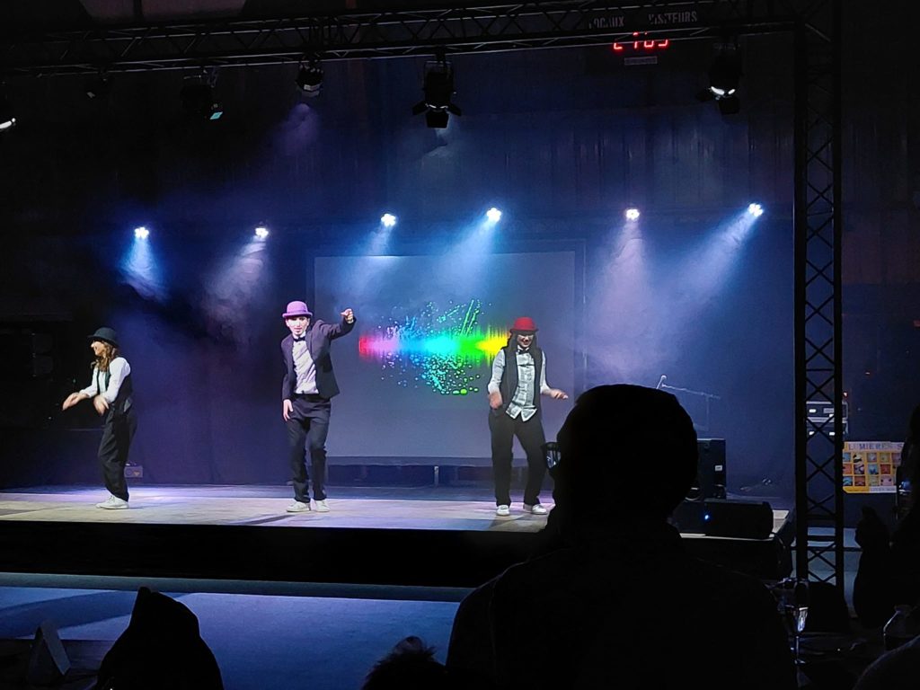 Danseurs en costume sur scène lors du Téléthon de Villepreux, éclairage coloré en arrière-plan.