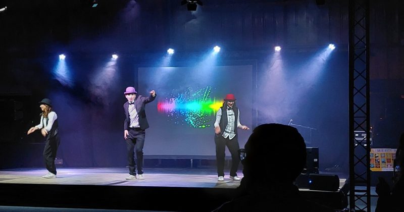 Danseurs en costume sur scène lors du Téléthon de Villepreux, éclairage coloré en arrière-plan.