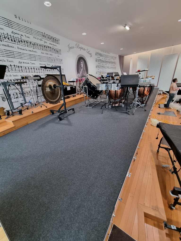Installation d'une scène fixe au conservatoire Jean Baptiste Lully avec praticables, moquette et instruments de percussion.