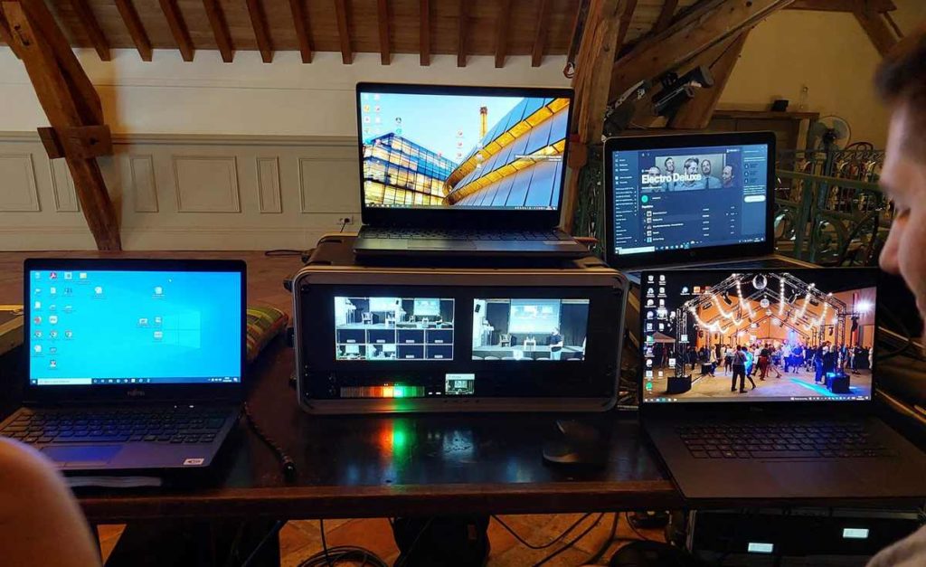Tableau de contrôle avec plusieurs ordinateurs portables et équipements audio-visuels pour un événement.