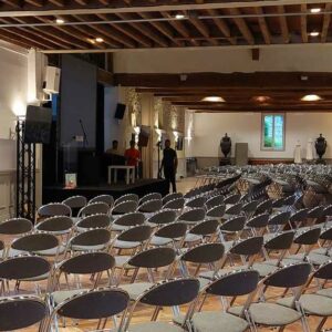Salle de conférence avec rangées de chaises, écrans et scène, préparée pour un événement le 17 mai 2022 par Symbiose Organisation.