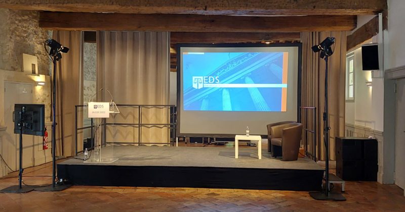 Scène de conférence avec un écran affichant "EDS", fauteuil et table, prête pour des réunions simultanées.