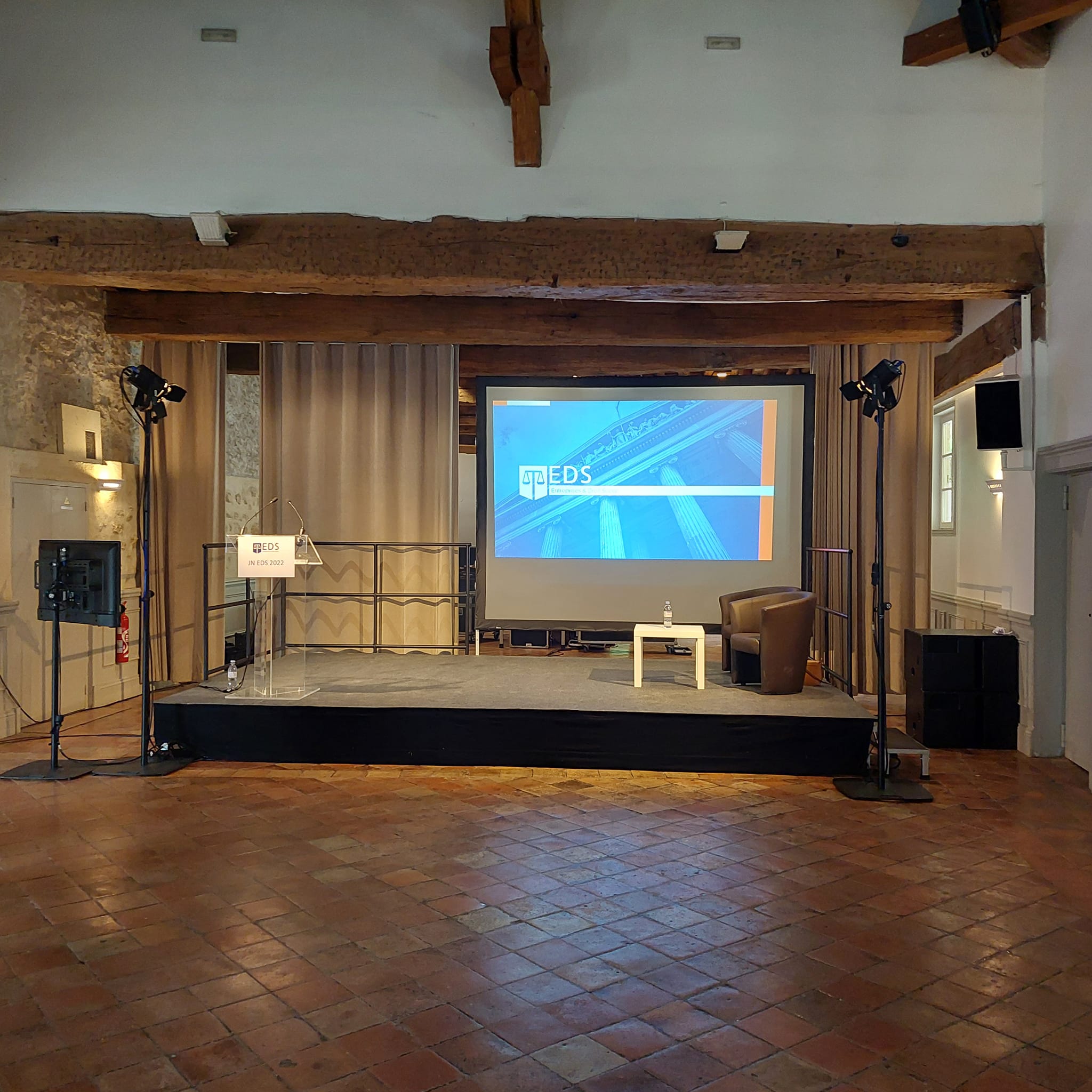 Scène de conférence avec un écran affichant "EDS", fauteuil et table, prête pour des réunions simultanées.